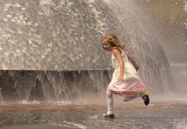 Young girl in her new dress, splashing in a founta...