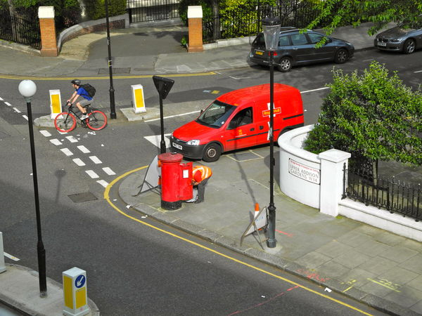 Postman collects the mail as a red wheeled bicycle...