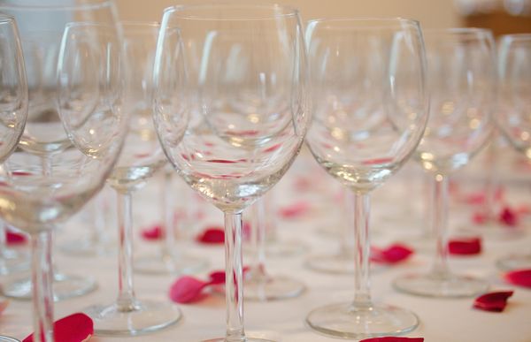 Wine glasses prior to a reception.  Scattered rose...