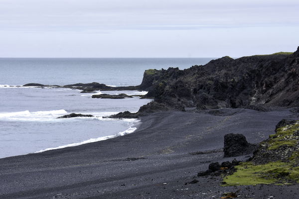Black sand beach. Wreckage visible at bottom right...