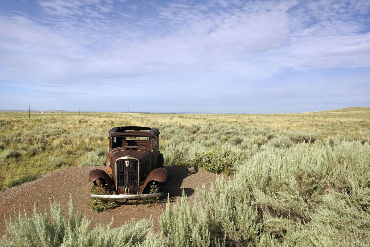 An old rusted-out car on an abandoned stretch of R...