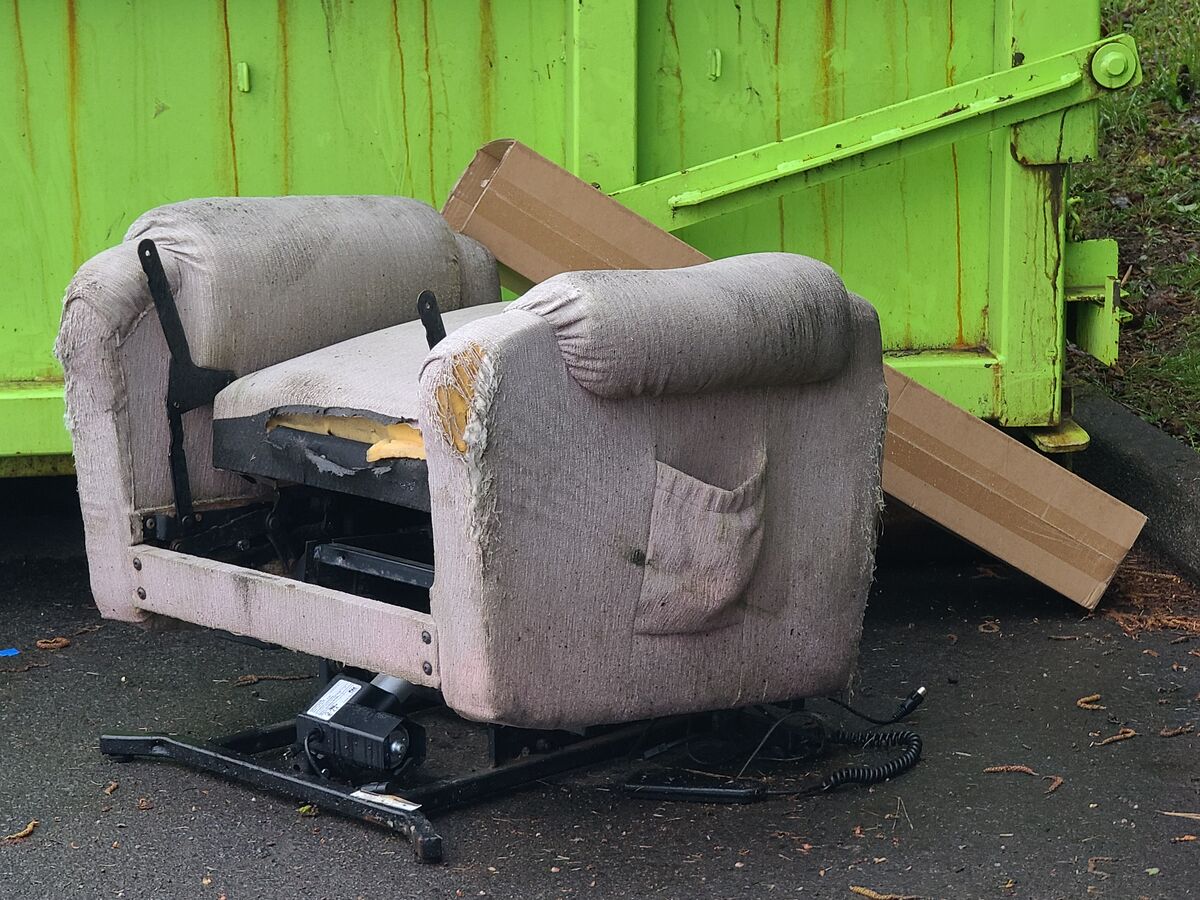 Dumpster with a broken easy chair beside it....